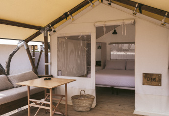 Interior de una tienda safari con suelo de madera, sofá, cama, mesa de madera y ambiente acogedor.