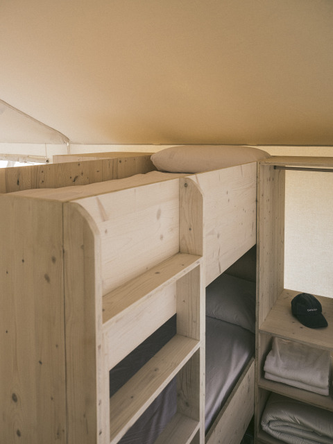 Letti a castello e scaffali in legno in una tenda safari chiamata «Cottage Family Tent» a Wecamp Cadaqués, Spagna.