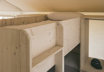 Literas y almacenamiento de madera en una tienda safari llamada «Cottage Family Tent» en Wecamp Cadaqués, España.