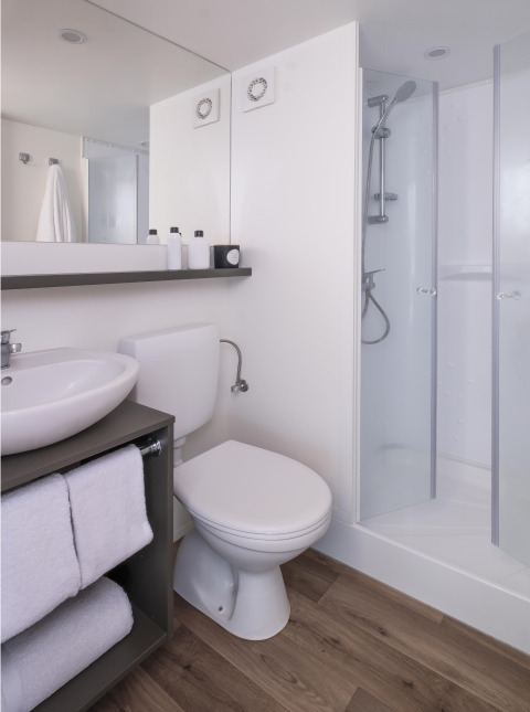 Baño moderno en tienda safari con ducha, inodoro, lavabo, espejo grande y toallas limpias sobre suelo de madera.