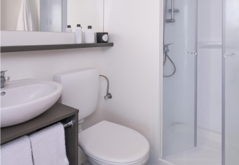 Bagno moderno in una tenda safari con doccia, WC, lavandino, specchio grande e asciugamani su pavimento in legno.