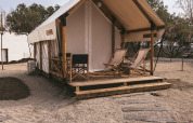 Safari-Zelt bei Wecamp Cadaqués in Spanien mit Holzveranda, Liegestühlen und Kieselsteinweg.