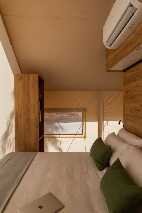 Safari-tent interieur met tweepersoonsbed, groene kussens, airco en warme houten accenten.