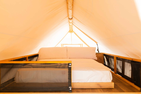 Interieur van een safaritent met een comfortabel bed, houten frame en zachte witte kussens onder canvas.