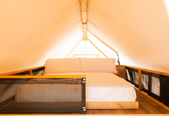 Vista interna di una tenda safari, con letto accogliente, struttura in legno e cuscini bianchi soffici.