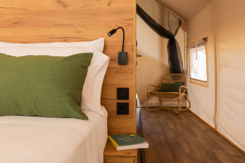 Interieur van een Glamping Comfort-safaritent met hout, groen kussen en stoel bij Wecamp Cadaqués.