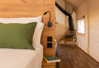Interieur van een Glamping Comfort-safaritent met hout, groen kussen en stoel bij Wecamp Cadaqués.