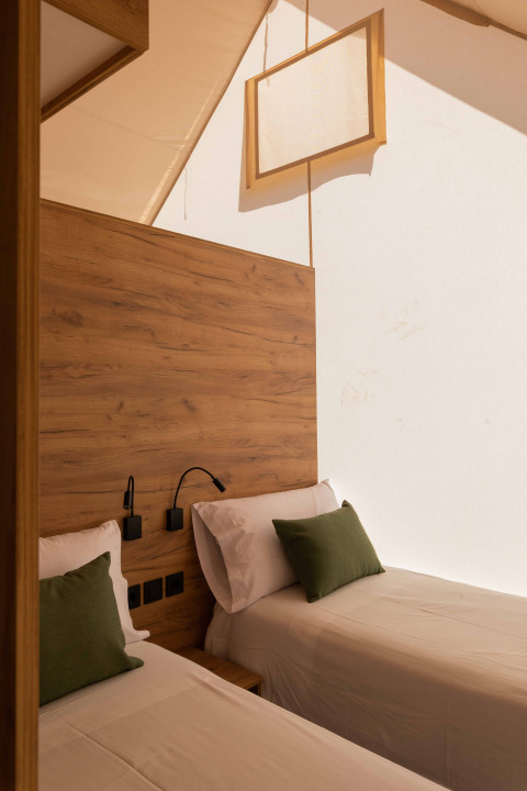Twee aparte bedden met groene kussens in een lichte safaritent bij Glamping Family Plus, Wecamp Cadaqués, Spanje.