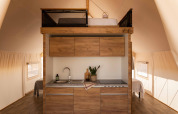 Cocina moderna con armarios de madera y cama tipo altillo en tienda Glamping Family Plus, Wecamp Cadaqués, España.
