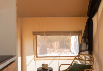 Interno della tenda safari Glamping Family Plus a Wecamp Cadaqués con sedia, tavolino e luce naturale.