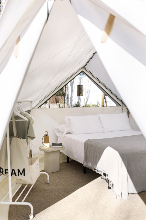 Innenansicht des Bell Tent Glamping mit Doppelbett, Nachttisch, Lampe und Kleiderständer.