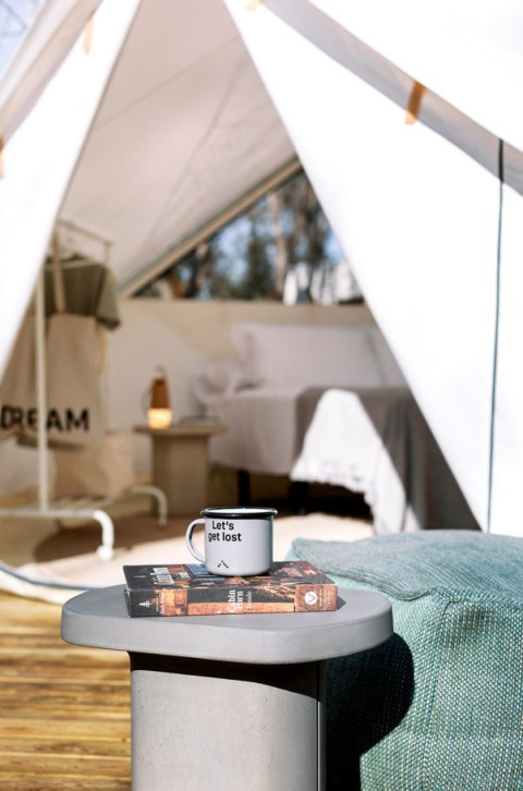 Safari telt ved Wecamp Cala Montgó med et lille bord, kop med teksten 'Let's get lost' og bog foran seng.