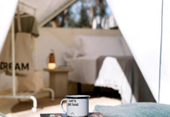 Safari tent at Wecamp Cala Montgó in Spain with table, mug reading 'Let's get lost', and book near bed.