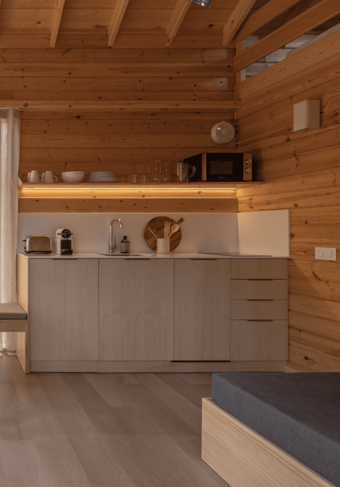 Pequeña cocina moderna con paredes de madera, estanterías abiertas y electrodomésticos compactos en bungalow.