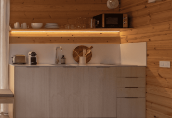 Pequeña cocina moderna con paredes de madera, estanterías abiertas y electrodomésticos compactos en bungalow.