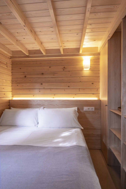 Dormitorio pequeño y acogedor en Bungalow «Duplex» de Wecamp Cala Montgó, con paneles de madera y cama doble.