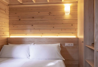 Dormitorio pequeño y acogedor en Bungalow «Duplex» de Wecamp Cala Montgó, con paneles de madera y cama doble.