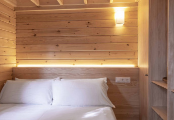 Dormitorio pequeño y acogedor en Bungalow «Duplex» de Wecamp Cala Montgó, con paneles de madera y cama doble.