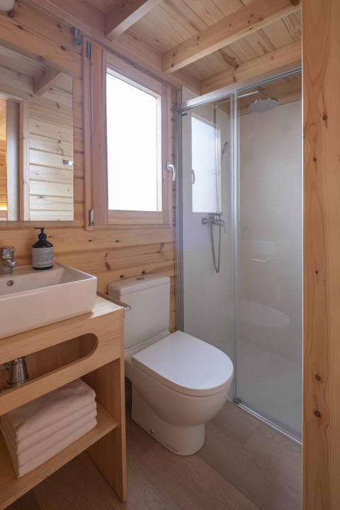 Baño moderno de madera con ducha, inodoro y lavabo en una pequeña casa en Wecamp Cala Montgó, España.