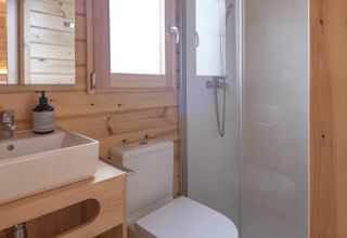 Baño moderno de madera con ducha, inodoro y lavabo en una pequeña casa en Wecamp Cala Montgó, España.