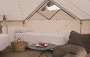 Innenraum des Bell Tent Plus Safari-Zelts mit zwei Betten, Sofa, Tisch mit Obst und Korb auf Teppich.