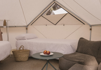 Innenraum des Bell Tent Plus Safari-Zelts mit zwei Betten, Sofa, Tisch mit Obst und Korb auf Teppich.