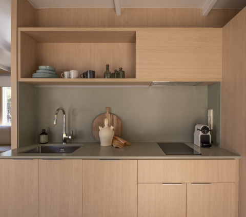 Coin cuisine de glamping moderne avec placards bois, étagères ouvertes, évier, plaque et machine à café.