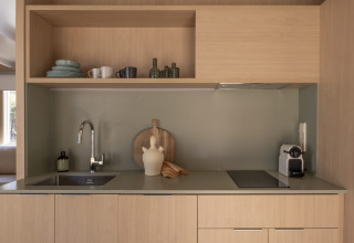 Moderne glampingkeuken met houten kasten, open planken, spoelbak, kookplaat, koffiezetapparaat en decoratie.