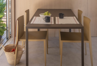 Eettafel in een tiny house met vier stoelen, twee mokken, een schaal druiven, placemats en een mand op de vloer.