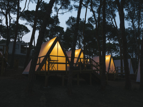 Tende safari illuminate al Wecamp Cala Montgó, Spagna, circondate da alberi al crepuscolo.