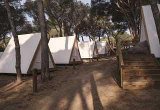 Tende safari triangolari immerse tra gli alberi a Wecamp Cala Montgó, Spagna, all’ombra della pineta.
