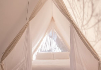 Vue intérieure d'une tente safari Cabin avec lit blanc au Wecamp Cala Montgó en Espagne.