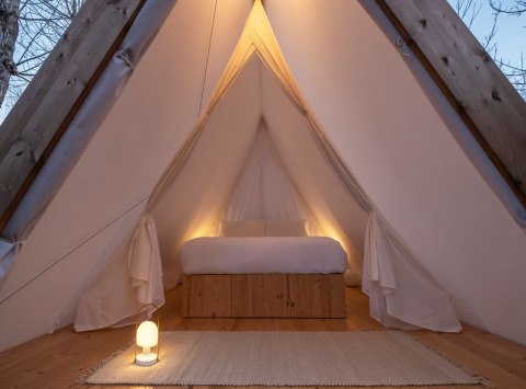 Interno della tenda safari Cabin Tent con letto comodo, decorazioni in legno e luce calda soffusa.
