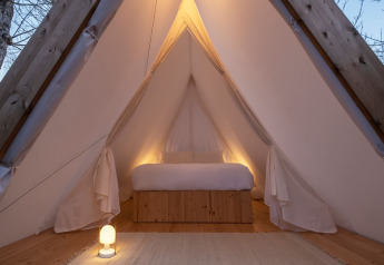 Intérieur de la tente safari Cabin Tent avec lit confortable, déco bois et lumière ambiante chaleureuse.