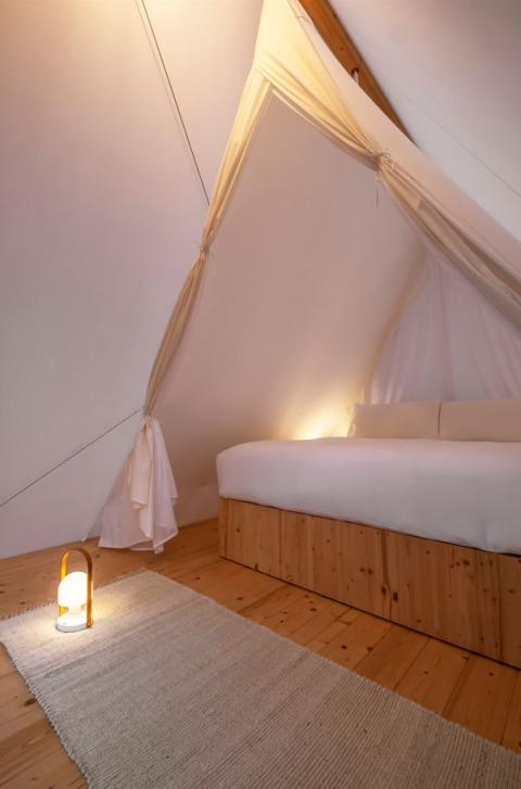 Interno della Cabin Tent al Wecamp Cala Montgó in Spagna con pavimento in legno, letto grande e luce soffusa.