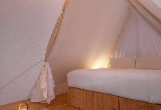Interno della Cabin Tent al Wecamp Cala Montgó in Spagna con pavimento in legno, letto grande e luce soffusa.