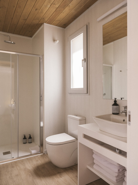 Modern, compact badkamer in een tiny house bij Wecamp Cala Montgó, Spanje, met houten plafond en glazen douche.