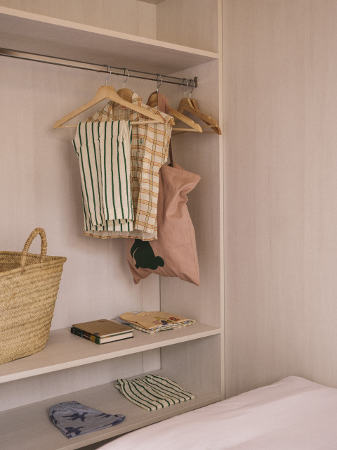 Minimalistische kast in een tiny house met hangende kleding, mand en boeken op de plank bij het bed.