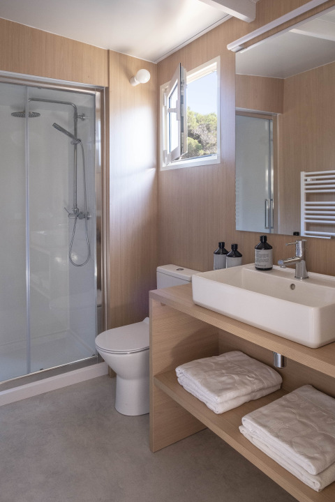 Moderne badkamer met douche, toilet, vierkante wastafel, open raam en handdoeken bij glampingverblijf.