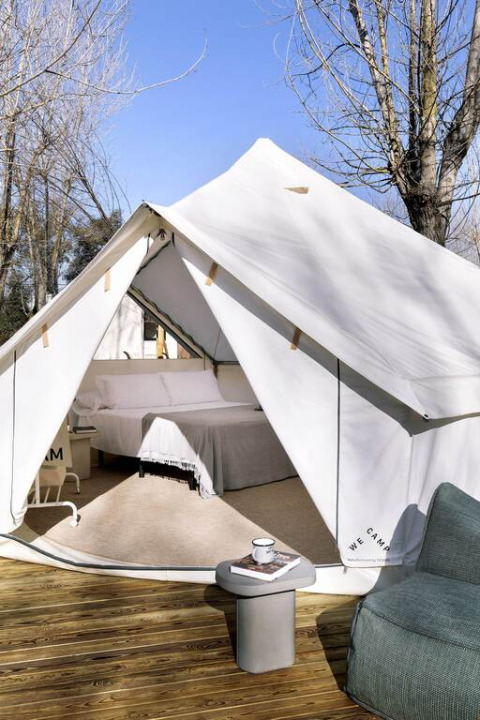 Photo d'une tente safari luxueuse avec lit double sur terrasse en bois et coin détente extérieur.
