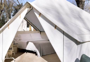 Foto eines luxuriösen Safarizeltes mit großem Bett auf einer Holzterrasse und Sitzmöbeln im Freien.