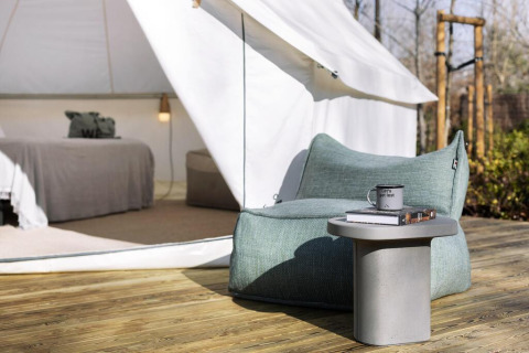 Safari tent with cozy lounge chair, small table, and visible bed inside, outdoor wooden deck, relaxing vibe.