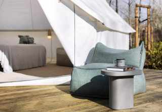 Tente safari avec fauteuil lounge, petite table et lit visible à l'intérieur, sur terrasse en bois extérieure.