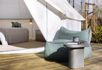 Safari-Zelt mit bequemem Sitzbereich, Tisch und Bett im Hintergrund auf einer Holzterrasse, entspannte Atmosphäre.