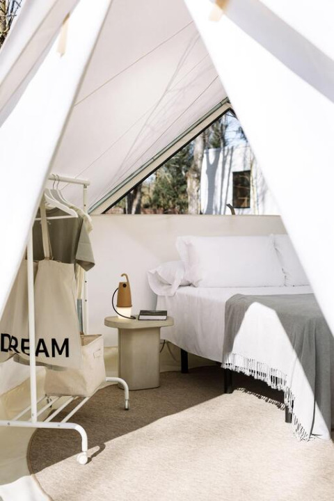 Interior view of a stylish safari tent with a cozy bed, clothing rack, side table, and soft daylight.