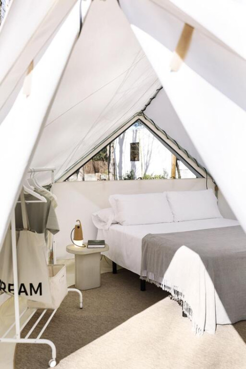 Vue intérieure d'une tente safari moderne avec lit confortable, table de nuit et portant à vêtements.