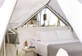 Vue intérieure d'une tente safari moderne avec lit confortable, table de nuit et portant à vêtements.