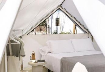 Vista interior de una tienda safari moderna con cama cómoda, mesita de noche y perchero cercano.