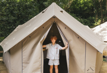 Un niño está en la entrada de una tienda safari Bell Tent sobre una plataforma de madera en un bosque verde.