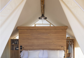 Binnenaanzicht van een safaritent met houten vloer, tweepersoonsbed en moderne inrichting in Spanje.